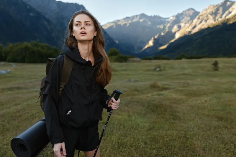A lone hiker stands outdoors in a rugged mountain landscape, wearing black hiking gear with a backpack and trekking pole, ready for adventure and exploration.