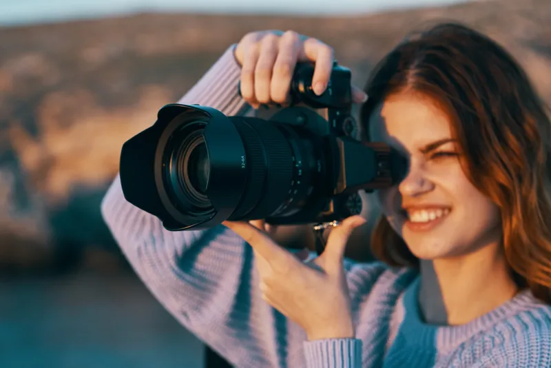 Счастливая женщина-фотограф с камерой в горах на природе, на заднем плане река