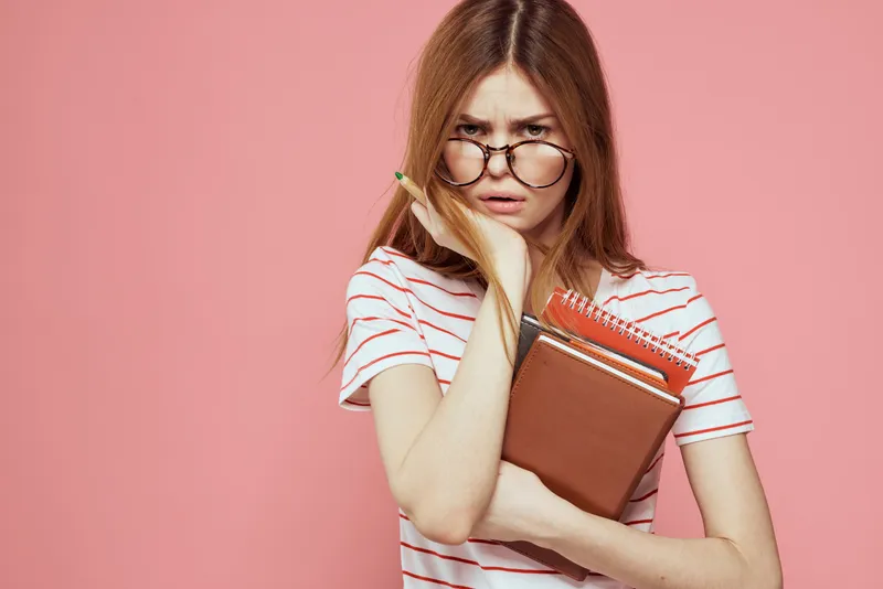 Молодая студентка с книгами на розовом фоне, в очках на лице, кадрированный вид, учебное заведение