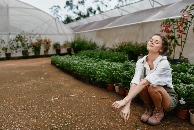 Young woman enjoying nature in a greenhouse, wearing casual clothes, surrounded by lush greenery and flowers, exuding tranquility and joy