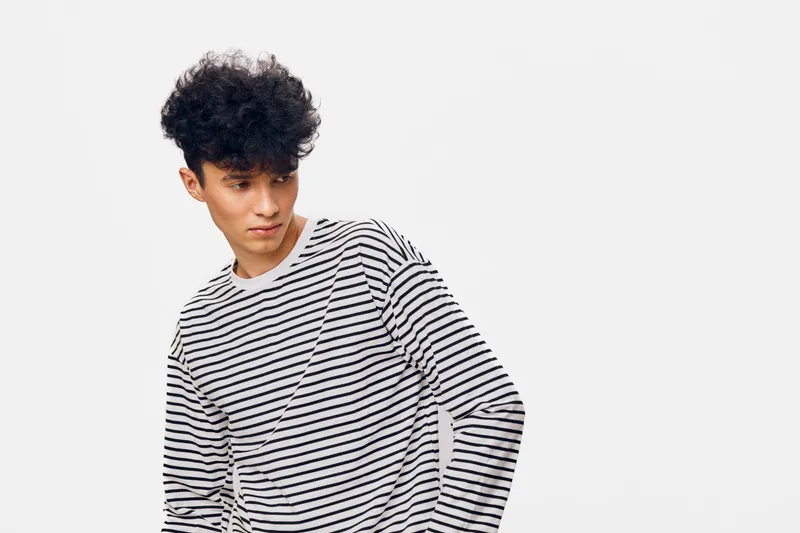 young man with curly hair wearing striped shirt looking sideways on white background, casual style, minimalistic fashion, studio portrait