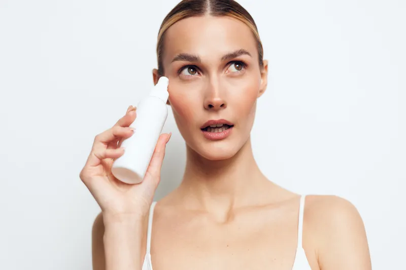 Young woman skincare beauty cosmetic serum bottle hygiene, white background, closeup portrait, holding small container near face, clean skin care routine