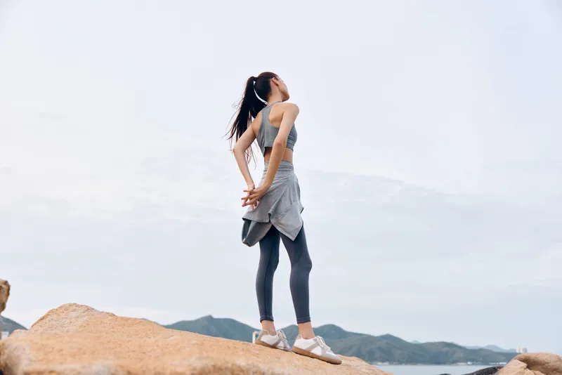 Young athletic woman in activewear enjoying serene outdoor scenery, practicing yoga or meditation, with mountains in the background