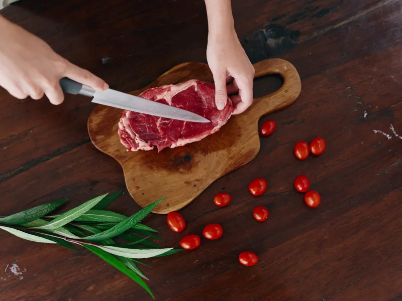 Женщина с ножом в руке нарезает свежее мясо стейка для жарки на кухне
