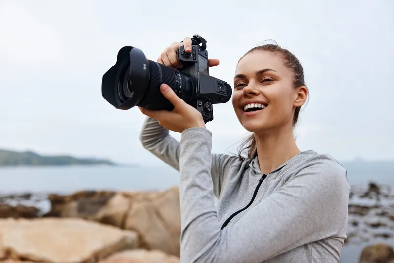 A cheerful female photographer capturing stunning coastal scenery with her camera, showcasing her passion for photography and the beauty of nature