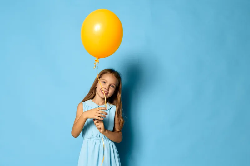 Веселая маленькая девочка держит ярко-желтый воздушный шар на ярком синем фоне с большим свободным пространством для текста