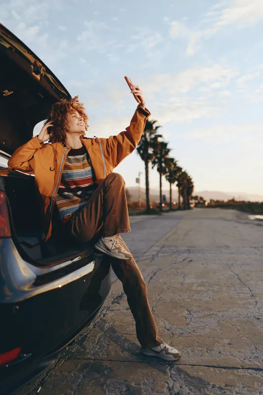 Woman lifestyle near car on road at sunset, smiling and posing with raised hands, casual outfit, relaxed traveler mood, golden light, cinematic outdoor travel scene for freedom feeling