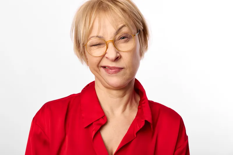 Woman portrait studio smile glasses red shirt senior blond face, relaxed expression, looking at camera, clean white background, soft lighting, calm mood