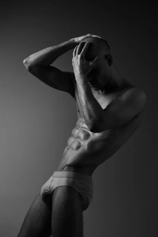 A striking black and white image of a man showcasing an expressive pose, highlighting his muscular physique and emotions through artistic lighting.
