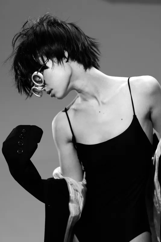 Black and white portrait of a woman with short hair wearing sunglasses and a black dress in an artistic pose.