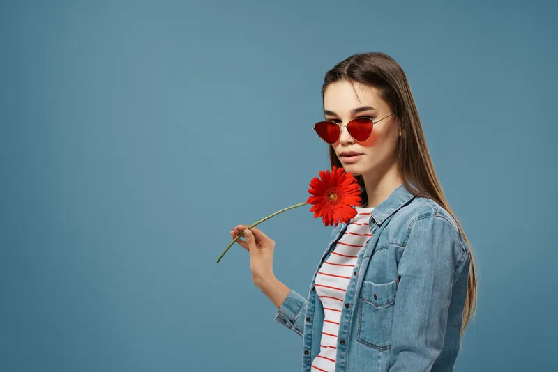 На фотографии изображена симпатичная брюнетка в солнцезащитных очках и с красным цветком
