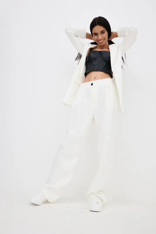 young woman smiling confidently in stylish white pantsuit and black crop top posing against plain white wall, modern fashion, casual elegance