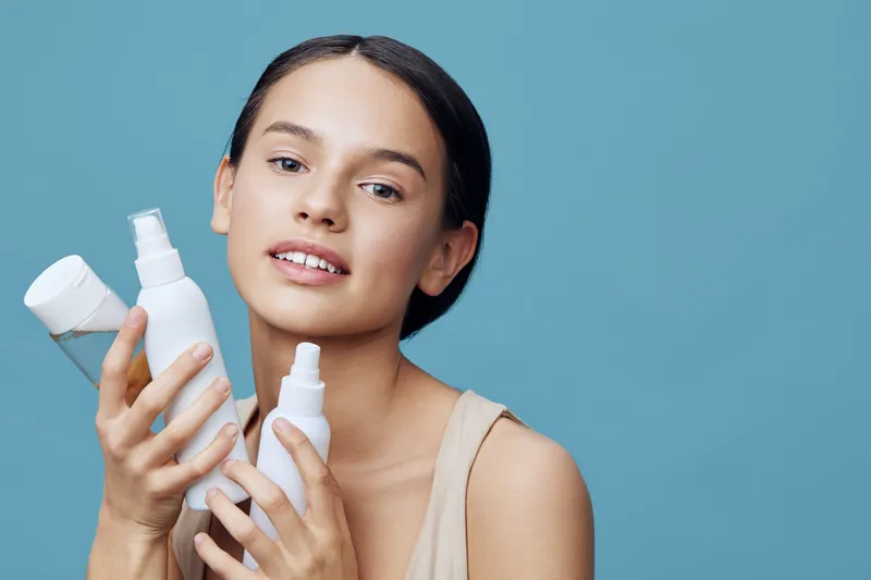 Young model holding skincare products with a bright blue background, showcasing healthy skin and beauty care routine, emphasizing hydration and self care