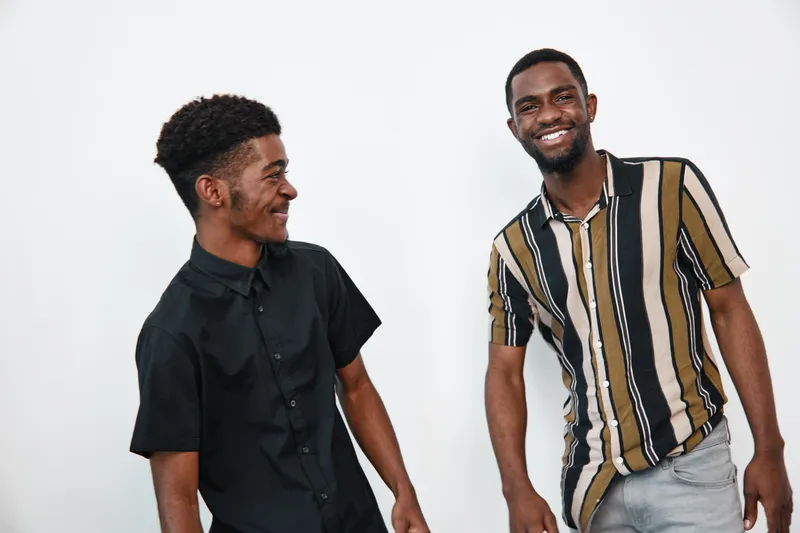Two young black men smiling and standing together in casual clothes on white background. African ethnicity, dark skin, friendship and happiness in studio portrait.