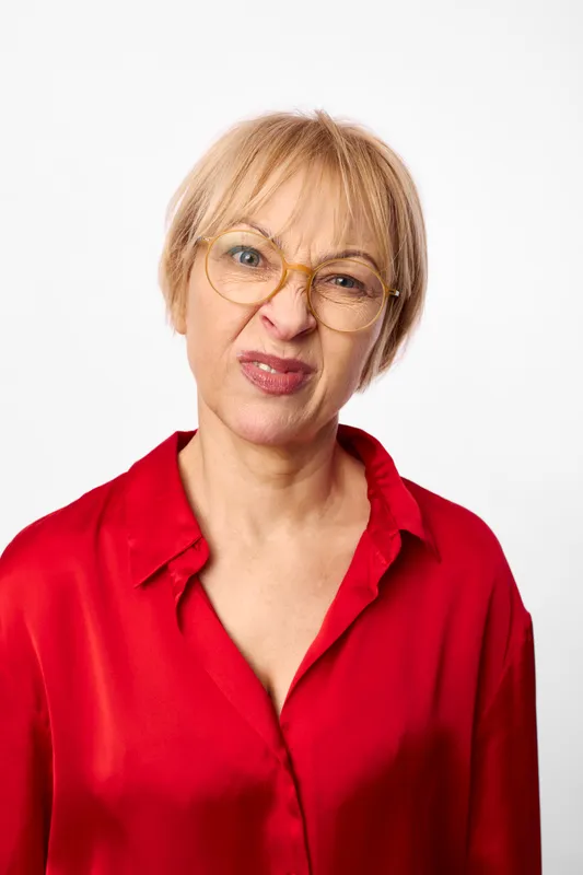 Senior woman portrait in red blouse and eyeglasses, facing camera with calm neutral expression, close headshot in studio light on a clean white background