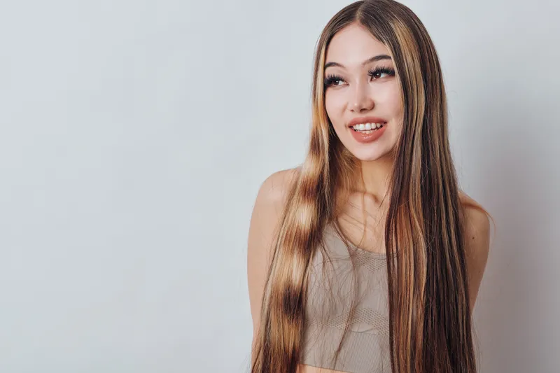 Young woman with long straight hair smiling and looking aside on plain background. Beauty, hairstyle, portrait, casual clothing and natural expression with positive mood.