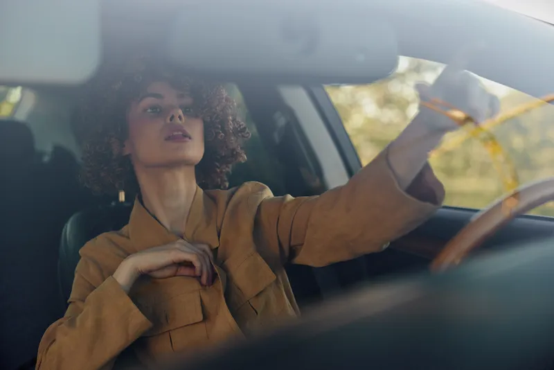 Woman driver sits inside a vintage car, wearing a brown shirt, relaxed pose, looking ahead, soft retro film color, afternoon light, lifestyle portrait, calm focus, candid moment, street driving vibe