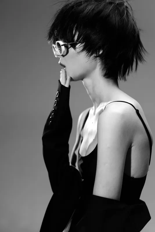 Black and white portrait of a thoughtful woman with short hair and glasses in stylish clothing.