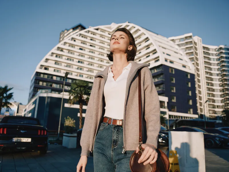 A cheerful professional stands in a sunny urban plaza, looking upward with a confident gaze. The scene conveys optimism, focus, and a dynamic city vibe.
