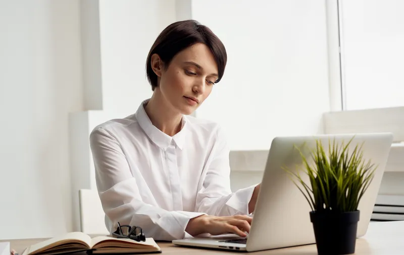 Женщина сидит за рабочим столом перед ноутбуком, она финансовый менеджер офиса