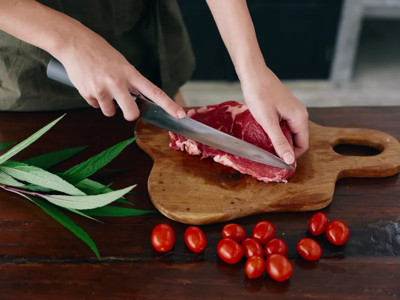 Женщина с ножом в руке нарезает свежее мясо стейка для жарки на кухне