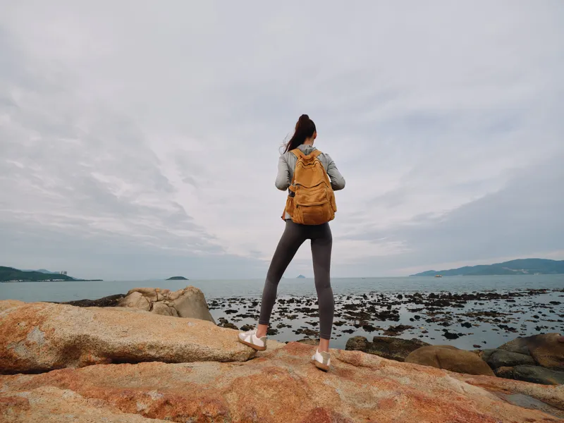 Woman in activewear exploring rocky coastline, wearing a backpack, enjoying nature and the ocean view, perfect for travel and adventure themes