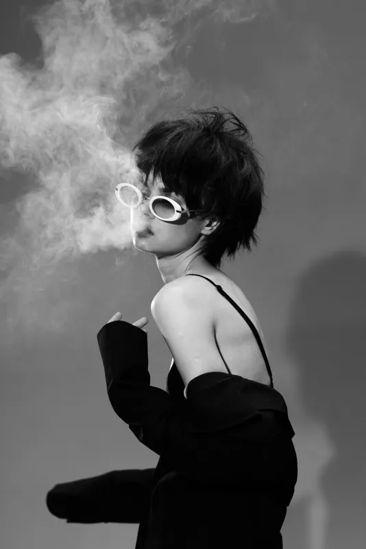 Black and white portrait of stylish woman smoking with white sunglasses and edgy hairstyle in studio lighting.