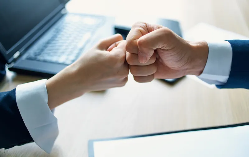 Сотрудники пожимают друг другу руки на работе в офисе, рядом документ о соглашении и ноутбук
