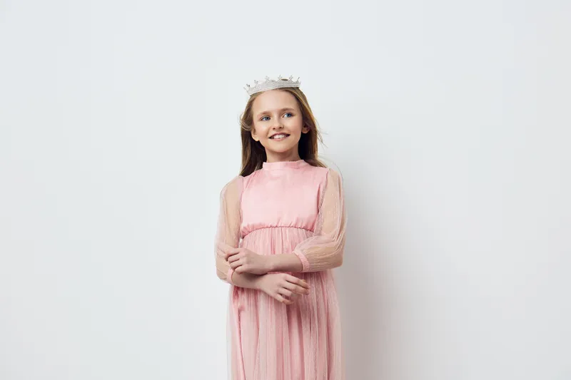 Happy young girl in a pink dress and crown, smiling against a light background, expressing joy and innocence, perfect for children s themes and celebrations