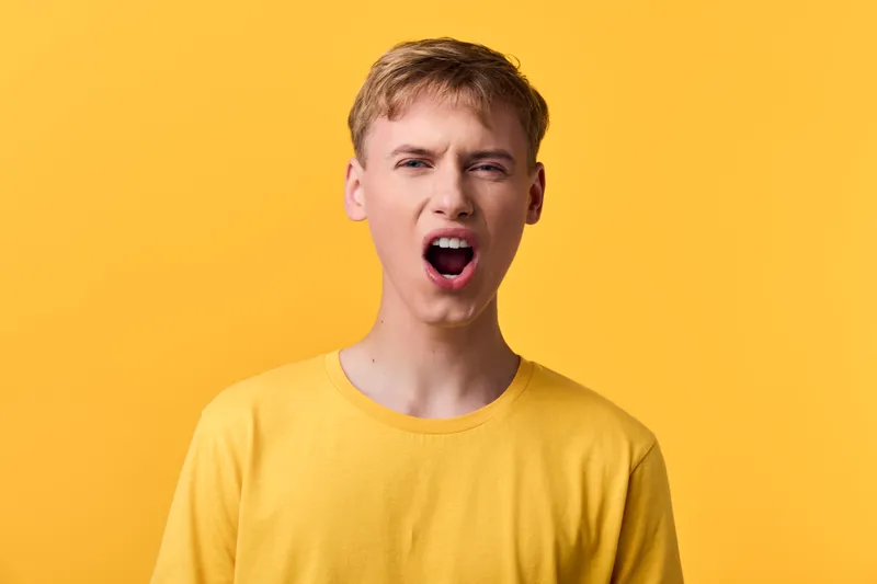 Yawning, mouth open, yellow background, yellow shirt, facial expression, energy in a studio closeup with bright lighting and vibrant color conveying bold emotion and casual fashion in a single shot