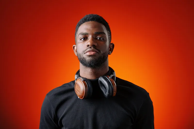 Confident young Black man with headphones against an orange background, representing passion for music and modern lifestyle, ideal for creative projects