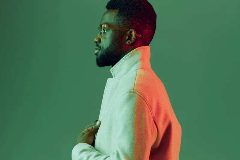 Thoughtful man in modern style poses against a green background, wearing a gray turtleneck and glasses, showcasing a contemporary and reflective mood