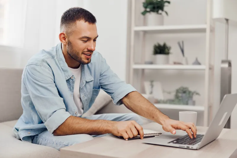 Smiling man engaging in remote work, showcasing a modern workspace. Dressed casually, he embodies productivity and comfort in a bright environment.