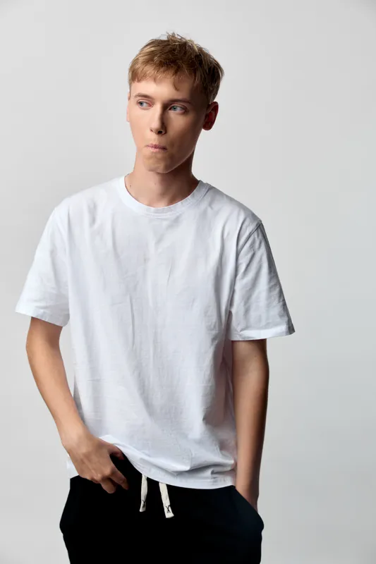 Casual male model wearing a plain white t shirt, relaxed stance with hands in pockets, studio lighting, clean background, simple fashion look