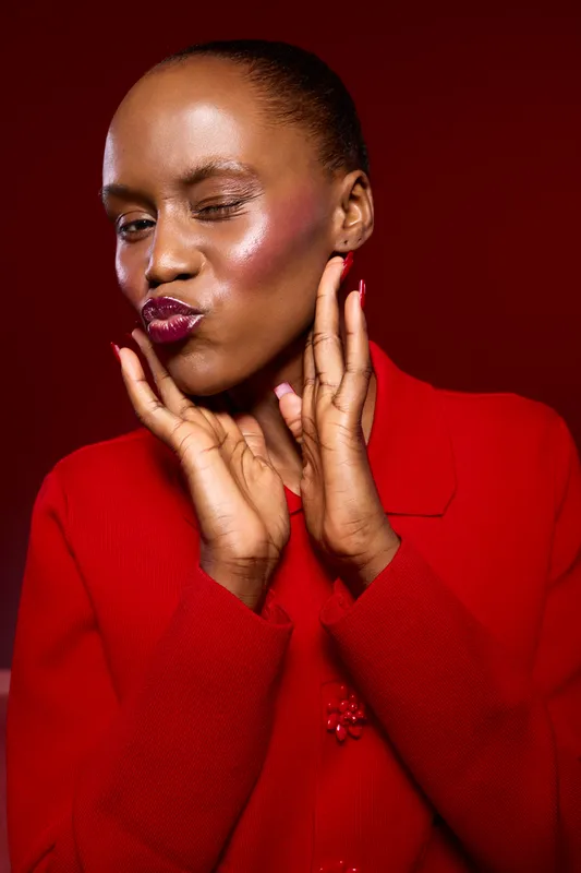 Portrait of a dark skinned African woman in red clothing making a playful face with puckered lips and hands near her face on a red background. Concept of beauty, fashion, and expression.