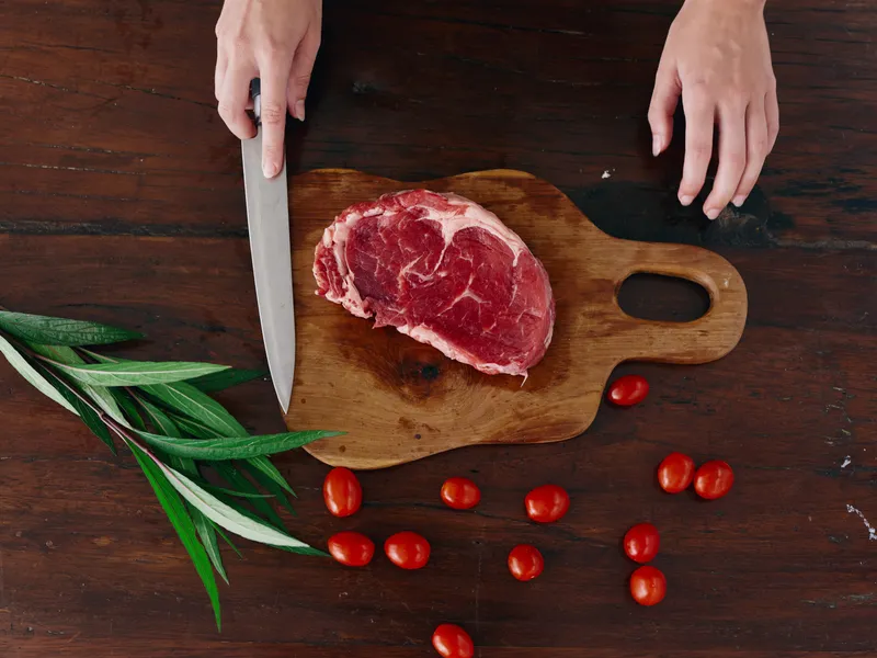 Женщина с ножом в руке нарезает свежий стейк из мяса для запекания на кухне