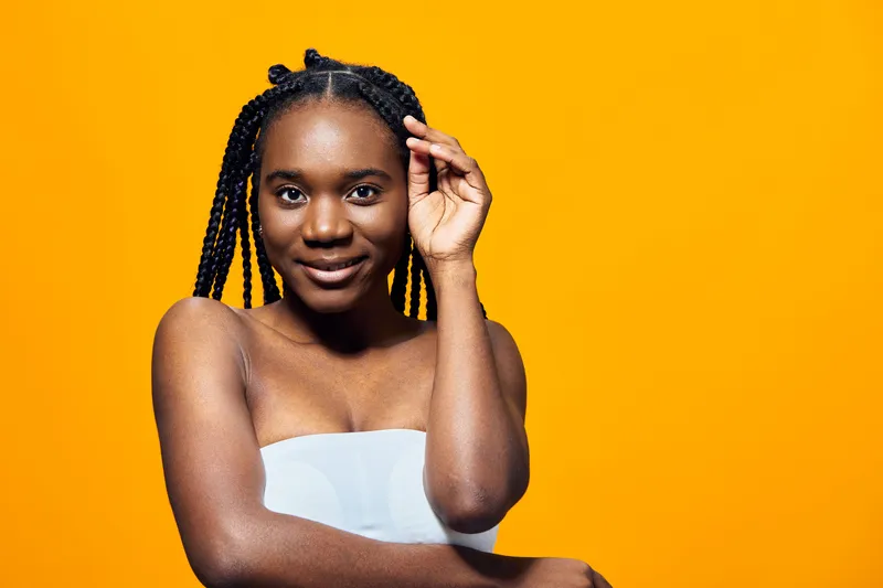 Young African woman with braided hair smiling against a bright yellow background, showcasing confidence and beauty in a natural portrait