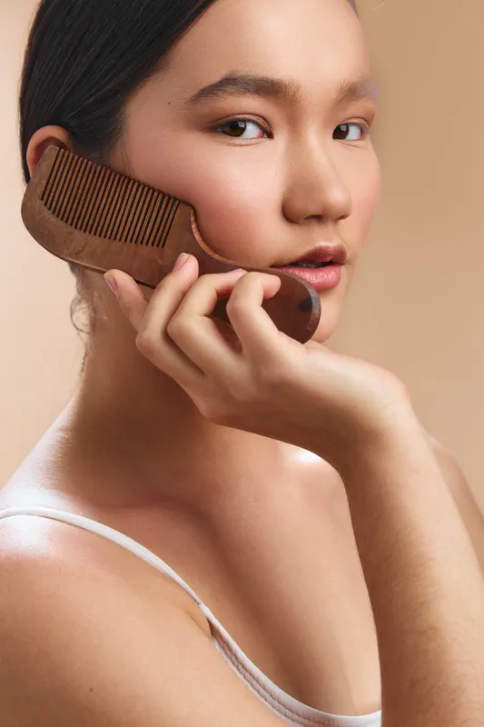 asian woman holds a vintage comb to her cheek in a soft intimate portrait. She carries calm elegance and a contemplative mood.