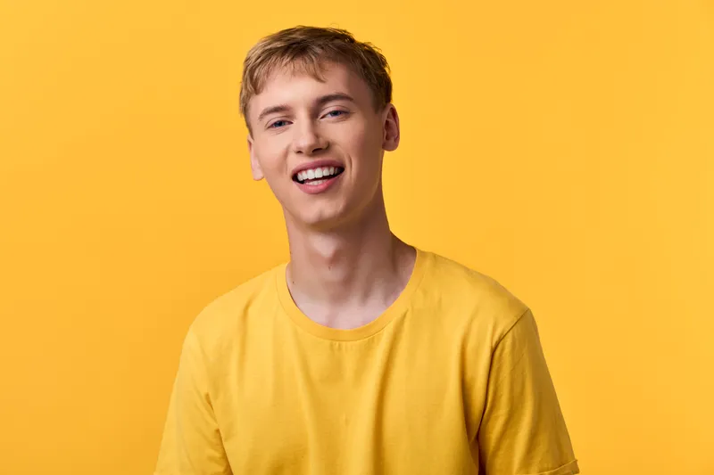 Smiling man in a yellow shirt stands against a vibrant yellow background, conveying casual style, warmth, and a cheerful mood for lifestyle and fashion projects.