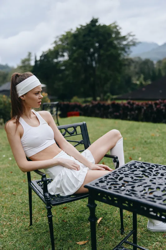 Young athletic woman in white sportswear sitting on a chair, showcasing a healthy lifestyle in a serene outdoor setting amidst greenery and mountains