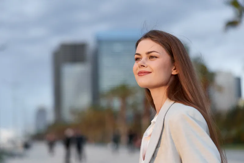 Confident businesswoman enjoying a sunset cityscape, showcasing professionalism and ambition amidst modern architecture.