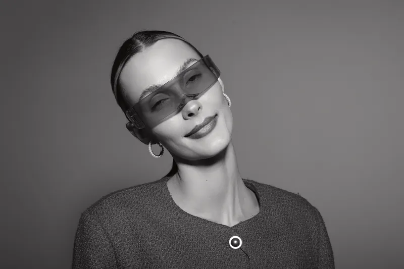 Portrait of a smiling white woman with pale skin wearing oversized sunglasses and hoop earrings in a studio. Concept of fashion and elegance.