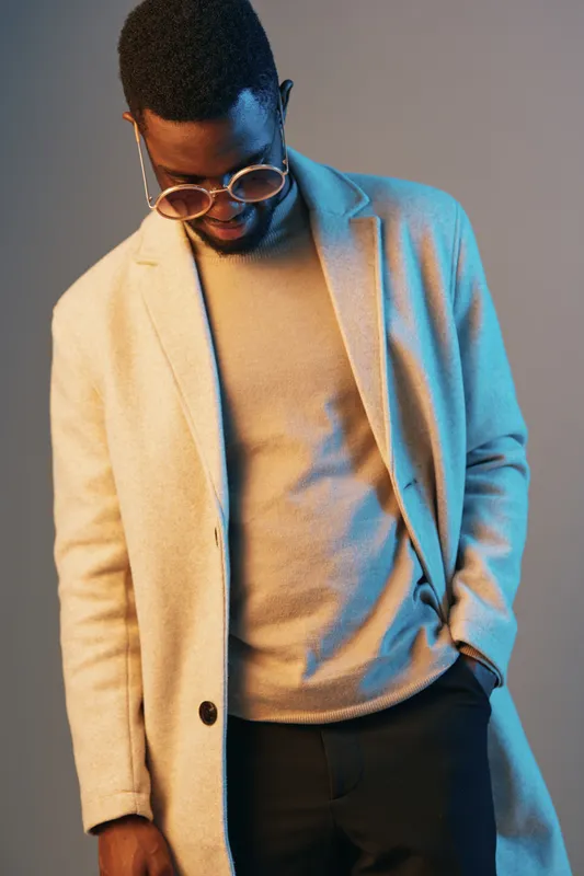 Stylish man in a fashionable beige coat, showcasing modern urban fashion with a confident pose against a gradient background Unique looks and trendy styles