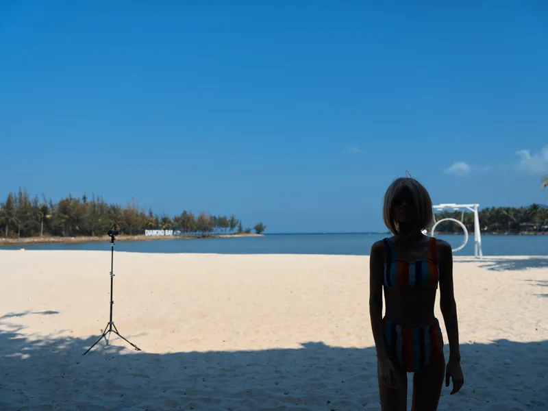 Silhouette of a young girl standing on a sunny sandy beach with calm blue sea and clear sky in the background, summer holiday atmosphere