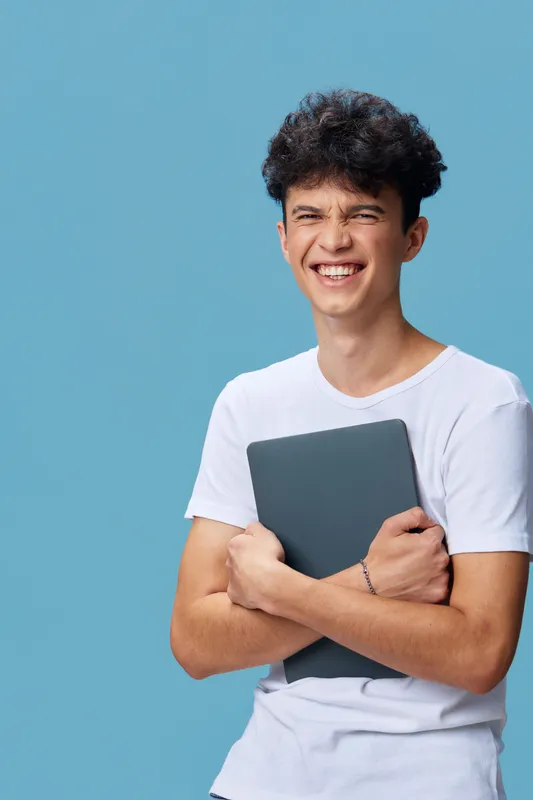 smiling man holding tablet, casual dressed young adult with curly hair, blue background, happy expression, modern technology device