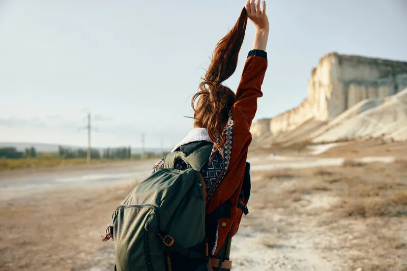 Авантюрная женщина празднует успех, стоя на удаленной грунтовой дороге с поднятыми в знак триумфа руками