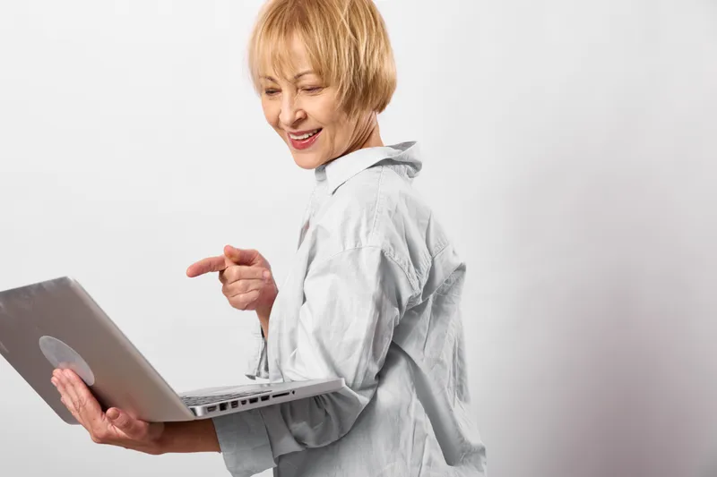 Woman using tablet, elderly smiling in studio setting, focused on touchscreen, modern technology for communication and digital learning, home browsing, light, calm mood