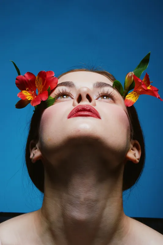 Beautiful young woman with flowers in her hair against a vibrant blue background, showcasing creativity and nature inspired beauty