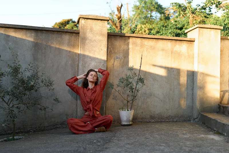 Woman in red sits on a rooftop terrace with hands behind her head. Outdoor lifestyle scene emphasizing relaxation, confidence, and casual living in warm, natural light