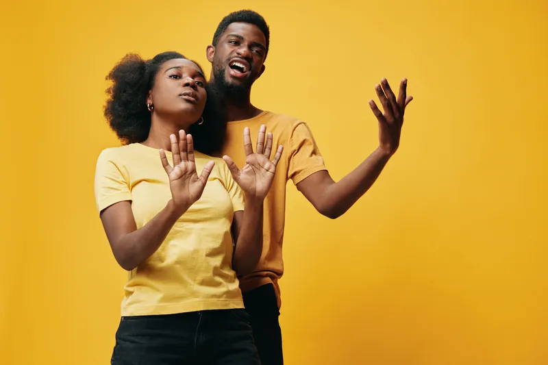 Young African American couple expressing joy and positivity against a vibrant yellow background, wearing matching casual outfits, showcasing emotional connection and happiness